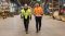 Two men in high visibility jackets stand in an industrial setting train depot