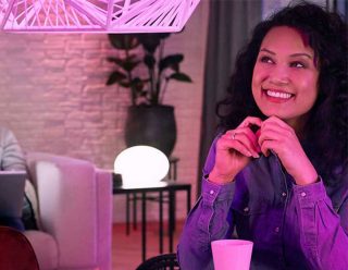 "La lampe suspendue DEL rose vibrante et la lumière intelligente de la table créent une ambiance ludique, illuminant l’expression ravie de la femme dans l’espace de vie moderne"