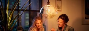 "Vintage-style LED filament bulb pendant illuminating two women enjoying evening conversation, creating warm ambiance in urban apartment."