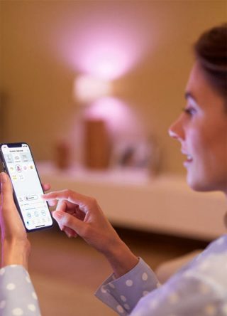 "Woman controlling smart LED lighting via smartphone app, adjusting pink ambient glow for personalized home atmosphere."