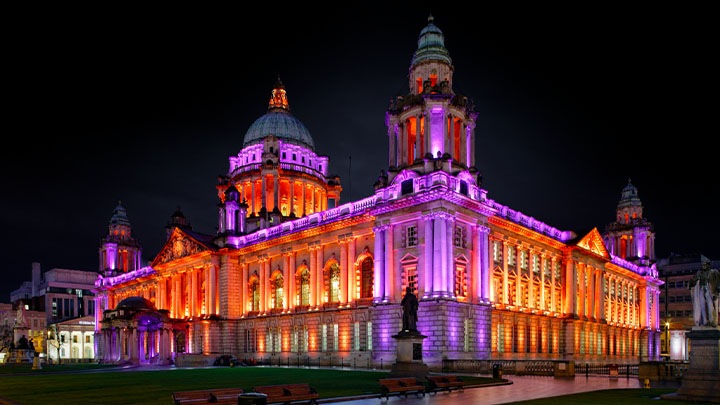 Belfast city hall at night, illuminated with purple and orange lighting