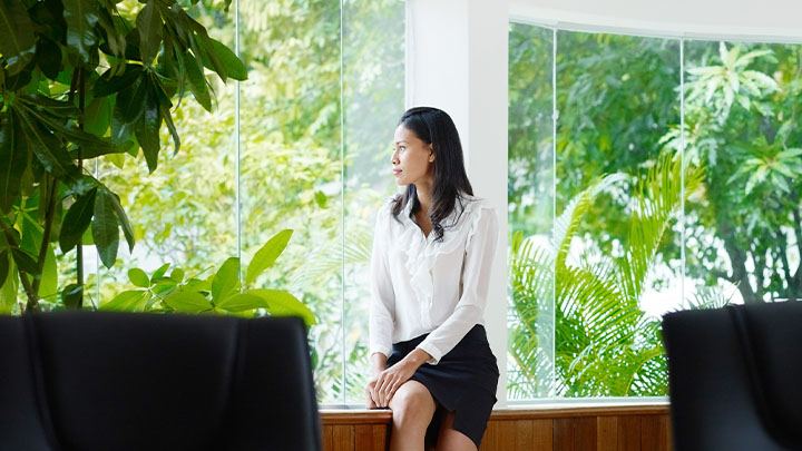 A woman looking out of a modern glass building to see a green natural landscape