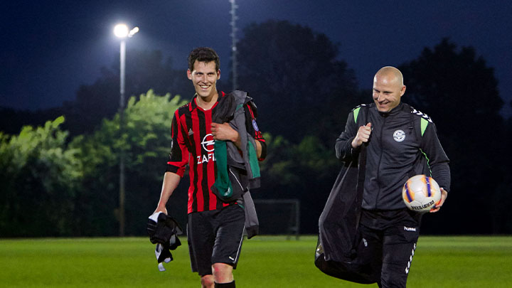 A football player and their coach walking off of the pitch smiling