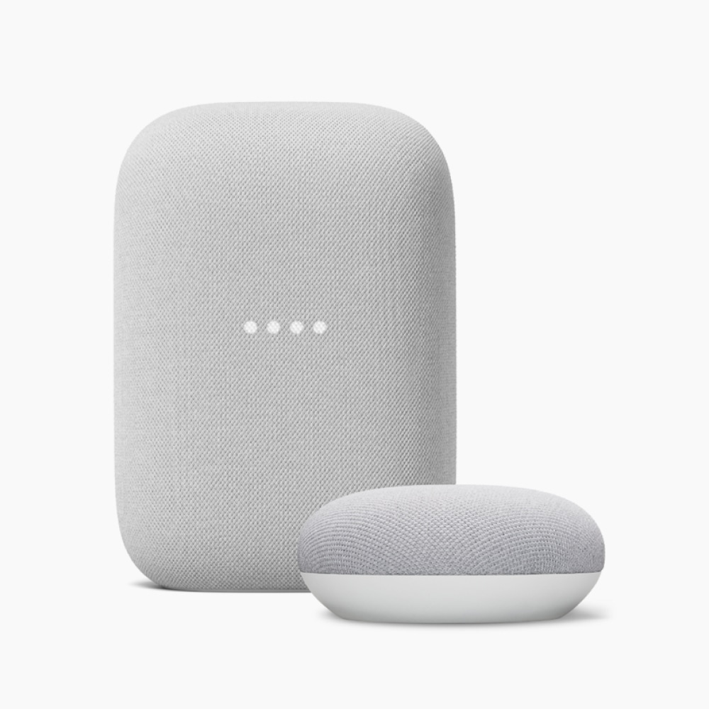 Two smart speakers in light grey fabric finish, one upright and one rounded, with four illuminated dots on the front.