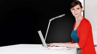 Mujer estudiando en un escritorio con lámpara de trabajo LED ajustable, que proporciona una iluminación óptima para la tarea en un colorido espacio de aprendizaje en el hogar.