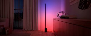 Une lampe de table à dégradé Signe Philips Hue disponible dans les soldes d’éclairage du Vendredi fou éclaire un mur dans des tons roses et bleus de lumière intelligente.