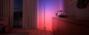 Un lampadaire gradient Philips Hue Signe, disponible dans l'offre d'éclairage Black Friday, baigne le mur d'une lumière connectée aux tons roses et bleus.