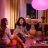 Deux personnes sont assises sur un canapé avec une lampe colorée au-dessus d'elles, tandis qu'une autre personne est assise à une table en arrière-plan.