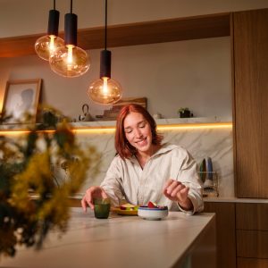 Une femme mange à une table avec des lampes Hue au-dessus d'elle et un lightstrip derrière elle.