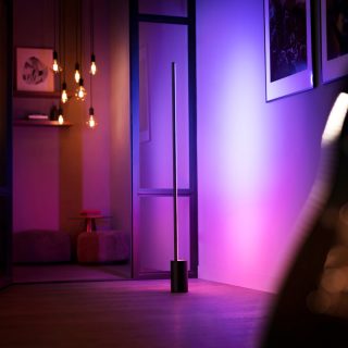 Un lampadaire Gradient Signe projette une lumière connectée rose et violette sur un mur.