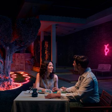 Un couple dîne sur la terrasse, entouré de lightstrips d'extérieur Neon qui entourent un arbre et un parterre de fleurs et diffusent une lumière rose. 