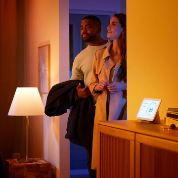 Un couple entre dans un salon baigné d'une lumière connectée blanche et chaude.