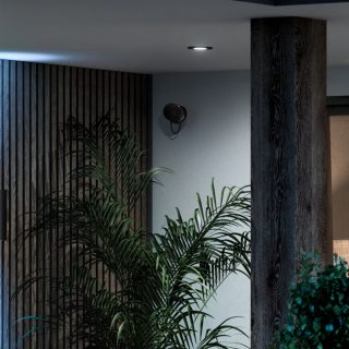Une caméra filaire Hue Secure surveille un espace extérieur éclairé par une lumière connectée, blanche et brillante.