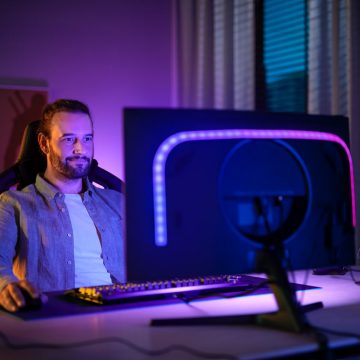 Un homme est assis devant un écran d'ordinateur équipé d'un Hue Play gradient lightstrip qui brille dans des tons bleus et violets. 