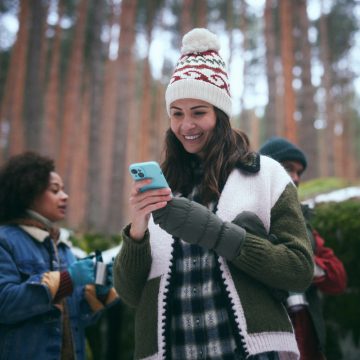 Glimlachende vrouw die haar smart home-beveiligingssysteem op haar smartphone bekijkt in het bos