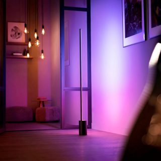 A Signe gradient floor lamp shining pink and purple smart light against a wall.