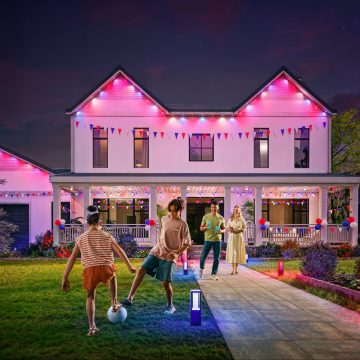 A family enjoy time in the front yard of their home with its façade illuminated with Festavia permanent outdoor lights glowing in red, white, and blue for a patriotic holiday theme. 