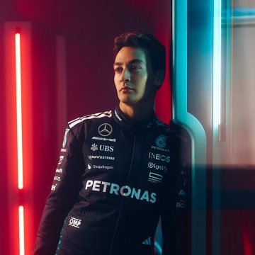 F1 Driver George Russell sits on a beige couch in a living room with soft, warm lighting.