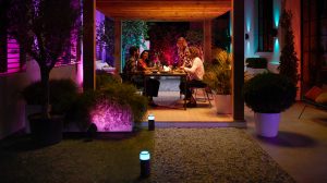 Quatre adultes assis à une table à manger d’extérieur avec un éclairage de paysage violet et bleu 