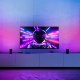 Deux lumières lèche-mur de jeux placées de chaque côté du téléviseur et brillant d’une vive lumière connectée rose et bleue.