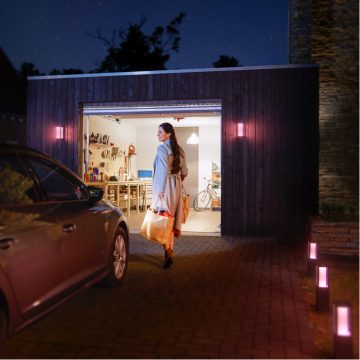 Une femme marchant de sa voiture à son garage bien éclairé en portant un sac d'épicerie