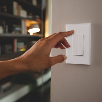Main sur le point d’allumer un interrupteur d’éclairage intelligent, blanc et mural