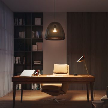Un espace de bureau à domicile avec un bureau et une chaise éclairés par une lampe de table et un luminaire suspendu connectés réglés dans des tons doux et chaleureux.