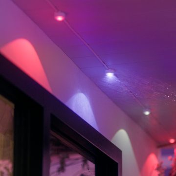 Une chaîne de lumières permanentes Festavia attachée au plafond d’un balcon avec des nacelles lumineuses qui brillent d’une lumière rose et violette.
