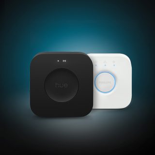 Nouveaux systèmes de commande de l’éclairage de maison intelligente Hue Bridge Pro et Philips Hue Bridge. Une personne qui contrôle l’éclairage intelligent Philips Hue à l’aide de l’application Hue sur un téléphone intelligent. Un Hue smart button blanc de Philips placé sur une table à côté d’un ordinateur portable.