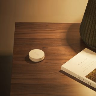Un Hue smart button blanc de Philips placé sur une table à côté d’un ordinateur portable.