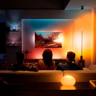 A couple watching TV with immersive TV surround lighting glowing in red, orange and yellow smart light.