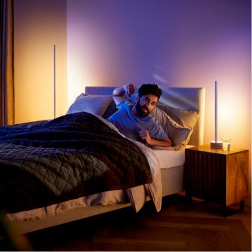 Un hombre que se estira en la cama con lámparas de mesa y de suelo inteligentes suavemente iluminadas 
