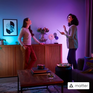  Two women standing in a living room with a purple wall looking up at the ceiling in amazement