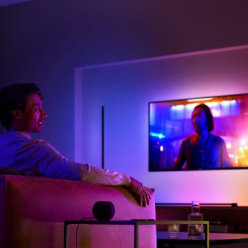 Man die op de bank tv kijkt met surroundverlichting en een slimme speaker op de bijzettafel naast hem