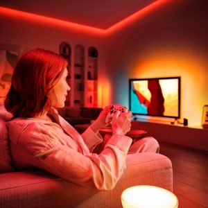 En kvinna spelar tv-spel medan väggen bakom tv:n lyses upp av ett fängslande ljus.