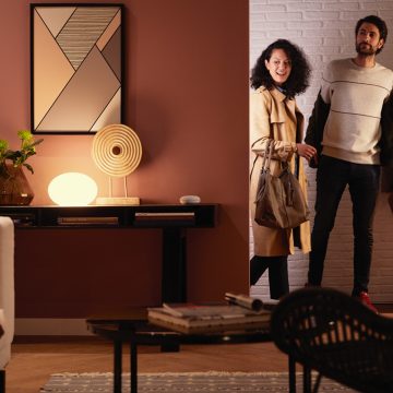 Ett par går in i vardagsrummet som är upplyst med en Philips Hue smart ljuskälla som lyser med varmvitt smart ljus.