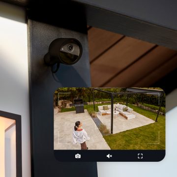 En Hue Secure kamera fäst på en vägg och en livebild från kameran som visar en kvinna i en trädgård.