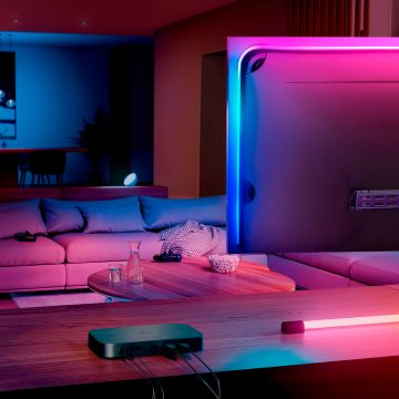 Hue sync box 8K sitter på ett konsolbord bredvid en TV-skärm i ett vardagsrum.