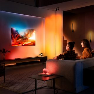 Par som sitter i soffan och tittar på tv med röda, oranga, gula lampor
