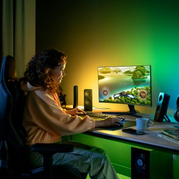Kvinna som sitter vid ett spelskrivbord med grön och gul Philips Hue smart belysning