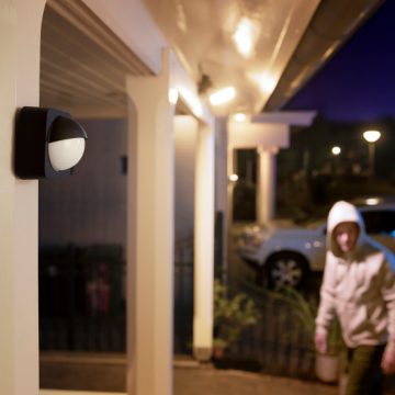En man närmar sig en ytterdörr upplyst av två vägglampor anslutna till en rörelsesensor utomhus.