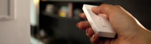 Hand pressing a button on a white dimmer switch labeled ""OFF,"" controlling smart lighting in a home environment.