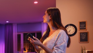 Person adjusting smart lighting in a living room using a mobile device, with colored lights illuminating the space.