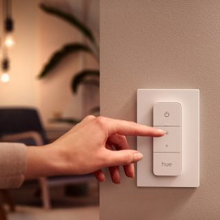 Finger pressing brightness button on a white smart lighting wall switch labeled ""hue"" to adjust light intensity in a home.