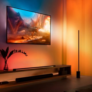 A collection of color-capable smart lights placed near a wall-mounted TV, casting synchronized colored light onto the wall.