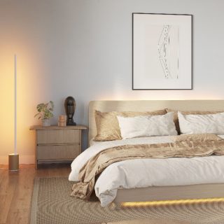 Tall smart floor lamp positioned beside a nightstand, casting amber light onto a bedroom wall and illuminating the bed frame.