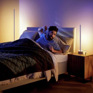 Person sitting up in bed, stretching, with bedside table lamps emitting soft, warm light in a modern bedroom setting.