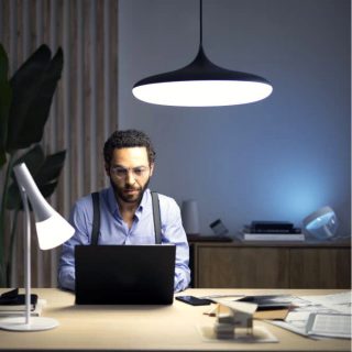 Person working at a desk with bright pendant and desk lights illuminating workspace, supporting focus in a modern home office setting.