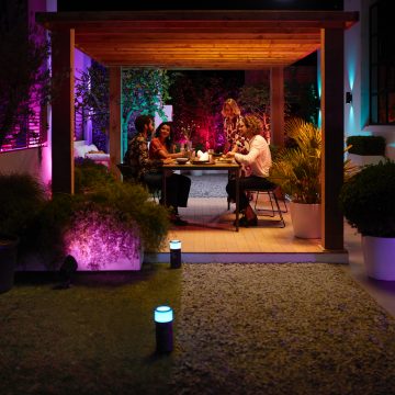 A group of friends dine outdoors surrounded by colorful smart lighting set to shades of purple and warm orange.