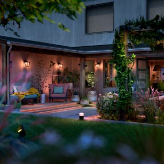 Outdoor smart wall lights and spotlights are installed around the backyard seating area, illuminating plants and pathways.